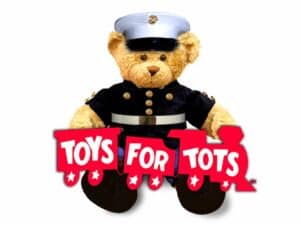 A teddy bear in Marine Corps dress blues holds a sign that reads Toys For Tots